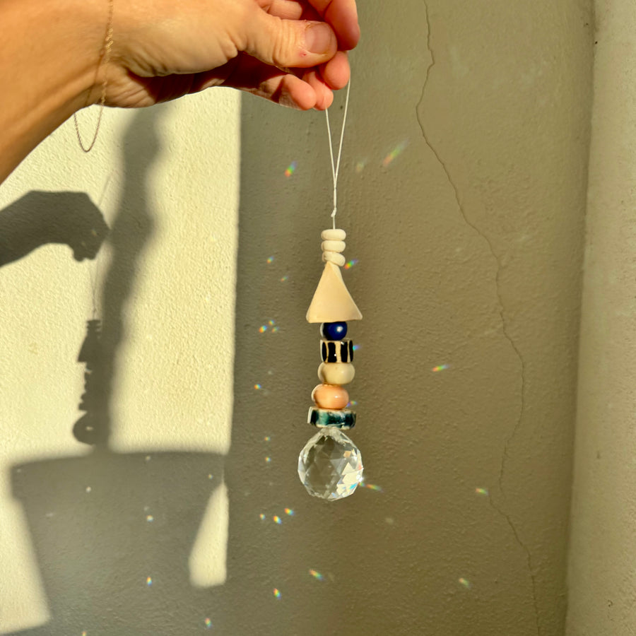 Hand holding a crystal hanging ornament with handmade ceramic beads against a neutral wall.