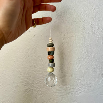 Hand holding a hanging crystal with colored beads against a white wall