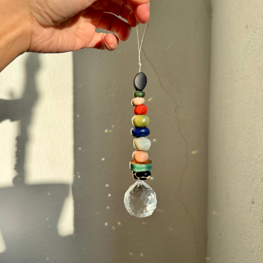 Hand holding a colorful beaded crystal hanging ornament against a neutral background
