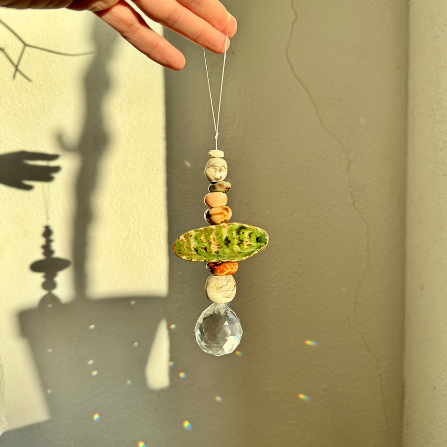 Hand holding a decorative hanging ornament with ceramic beads and a crystal against a neutral background