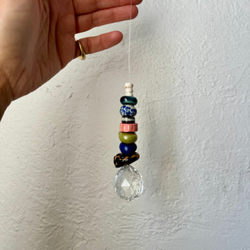 Hand holding a beaded hanging ornament against a white wall