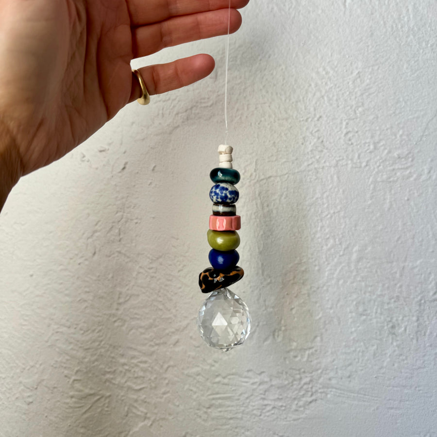Hand holding a beaded hanging ornament against a white wall