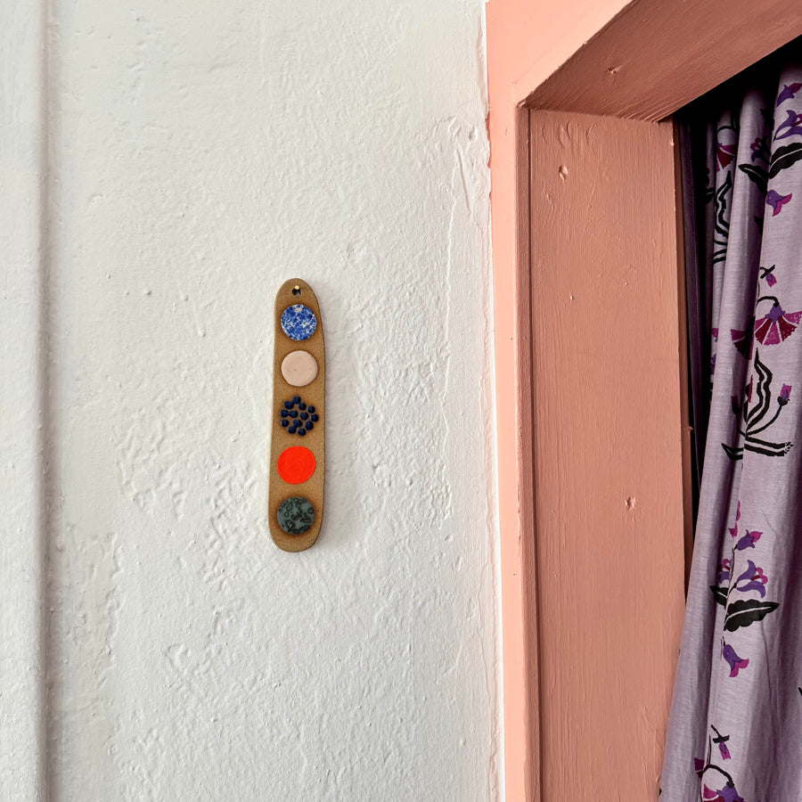 Decorative ceramic wall hanging with colorful circles on a white wall next to a door.