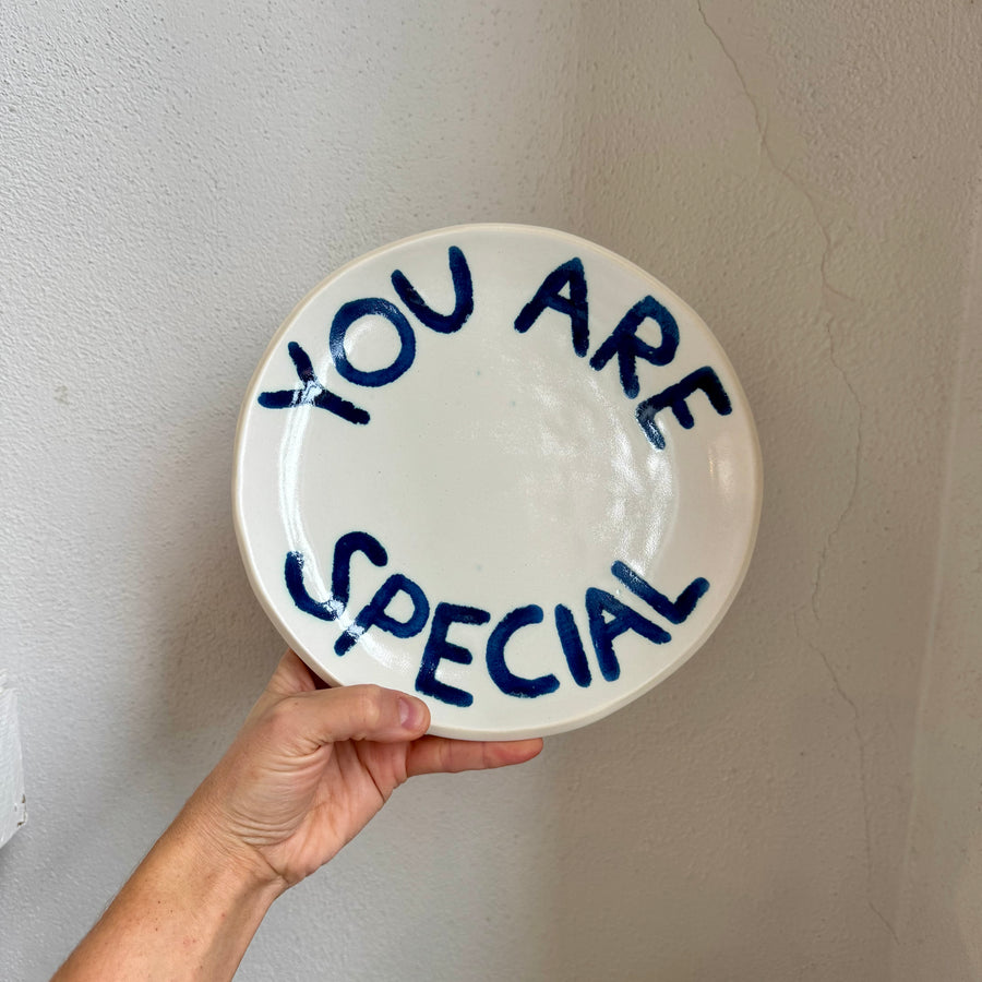White plate with 'YOU ARE SPECIAL' text held against a plain wall.