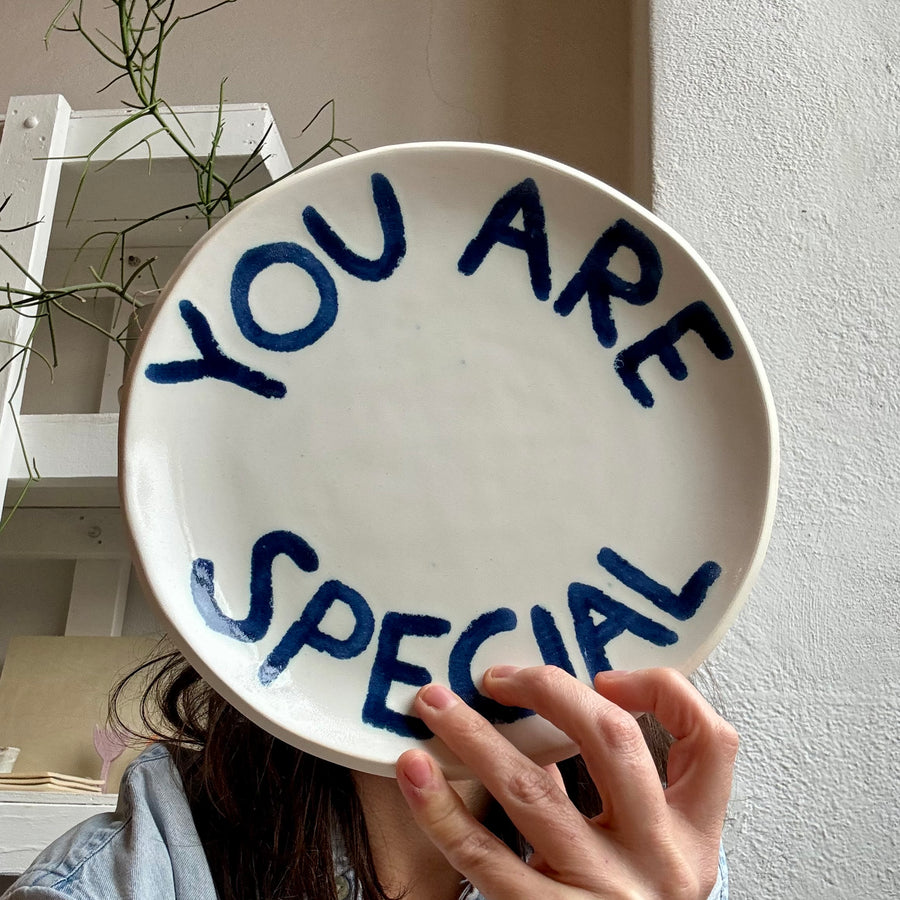 Person holding a white plate with 'YOU ARE SPECIAL' glazed in blue text.